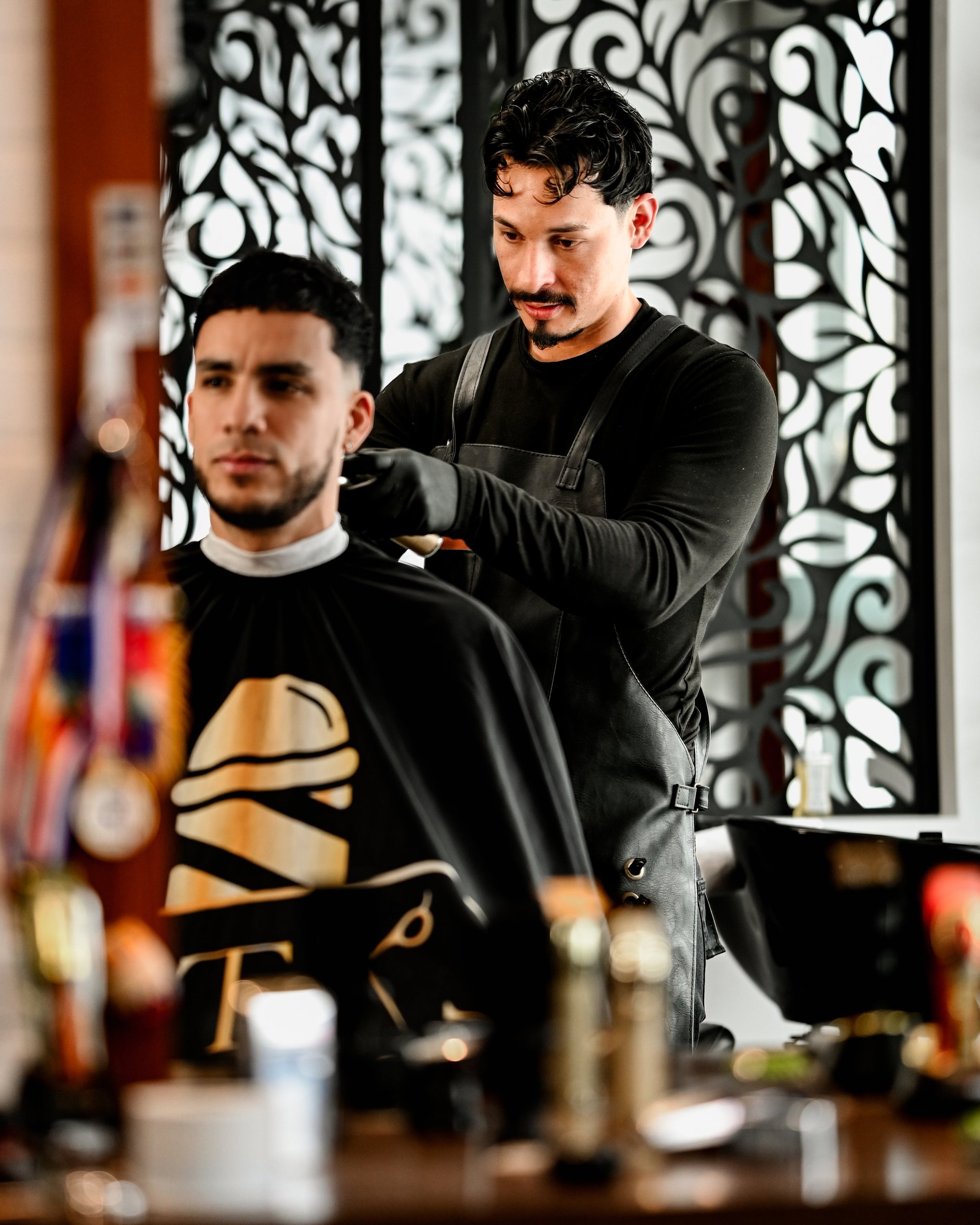 Barber styling a clients hair in a salon with decorative black and white wall panel in background